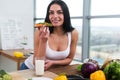 Close-up portrait of woman standing in kitchen, leaning on wooden table, having snack. Smiling girl maintains healthy Royalty Free Stock Photo