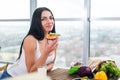 Close-up portrait of woman standing in kitchen, leaning on wooden table, having snack. Smiling girl maintains healthy Royalty Free Stock Photo