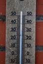 A close up portrait of a wooden mercury thermometer indicating the outdoor temperature in degrees celcius and is hanging on a red