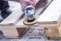 Close up portrait of workers hands at carpenter workspace refining the surface of wood board using sand paper grinder