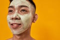 Close up portrait of young asian man with green mask applied on his face smiling away isolated over yellow background Royalty Free Stock Photo