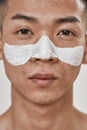 Close up portrait of young asian man with problematic skin and hyperpigmentation applied mask on his face, looking at