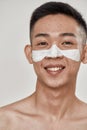 Close up portrait of young asian man with problematic skin and hyperpigmentation applied mask on his face, smiling at