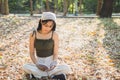 Close up portrait young Asian woman in casual wear sitting on floor with dry leaves reading a book in a public park Royalty Free Stock Photo