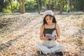 Close up portrait young Asian woman in casual wear sitting on floor with dry leaves reading a book in a public park Royalty Free Stock Photo