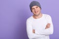 Close up portrait of young attractive man wearing white casual long sleeve shirt and gray cap, posing over lilac