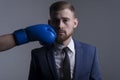 Close-up portrait of a young bearded guy in a business suit, businessman, side view the hand of an opponent in a boxing glove Royalty Free Stock Photo