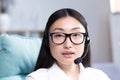 Close-up portrait of a young beautiful asian woman with glasses smiling and looking at the camera, uses a headset for video Royalty Free Stock Photo