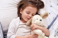 Close up portrait of young beautiful darkhaired girl, little princess with long hair, keeps eyes closed, child lies in bed, Royalty Free Stock Photo