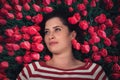 Close up portrait of young beautiful girl woman with red brown hair lying on grass with red tulip flowers around her Royalty Free Stock Photo