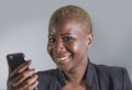 Close up portrait of young beautiful and happy trendy black afro american woman holding and using mobile phone isolated on grey ba Royalty Free Stock Photo