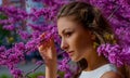 Close up portrait of young beautiful woman with brown hair in white dress poses elegant in blossom pink Judas tree Royalty Free Stock Photo