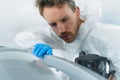 Close-up portrait of a young car painter checking the quality of automobile bumper paintwork.