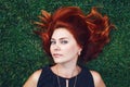 Close up portrait of young Caucasian beautiful girl woman with red brown hair lying on green grass in park. View from above Royalty Free Stock Photo