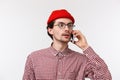 Close-up portrait of young caucasian man in glasses and red beanie, having conversation, calling friend looking around