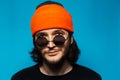Close-up portrait of young cheerful guy looking up, wearing orange hat and sunglasses on blue background. Royalty Free Stock Photo