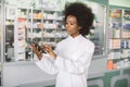 Close-up portrait of young confident pretty African woman doctor or pharmacist using digital tablet while standing in Royalty Free Stock Photo