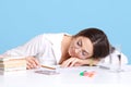 Close up portrait of young dark haired woman sitting at white desk, student sleeping and lying on her books, female tired of long