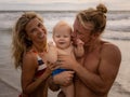 Close up portrait of young family spending time on the beach. Father and mother holding infant baby boy. Mom smiling, dad kissing Royalty Free Stock Photo