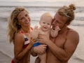 Close up portrait of young family spending time on the beach. Father and mother holding infant baby boy. Mom smiling, dad kissing Royalty Free Stock Photo