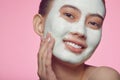 Close up portrait of a young female asian model applying clay face mask on a pink isolated. Royalty Free Stock Photo