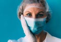 Close-up portrait of young female doctor in medical cap, mask, white gown and gloves on blue background. Royalty Free Stock Photo