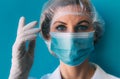 Close-up portrait of young female doctor in medical cap, mask, white gown and gloves on blue background. Royalty Free Stock Photo