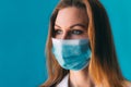 Close-up portrait of young female doctor in medical mask and white gown on blue background. Royalty Free Stock Photo