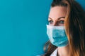 Close-up portrait of young female doctor in medical mask and white gown on blue background. Royalty Free Stock Photo