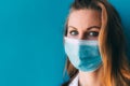 Close-up portrait of young female doctor in medical mask and white gown on blue background. Royalty Free Stock Photo