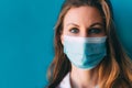 Close-up portrait of young female doctor in medical mask and white gown on blue background. Royalty Free Stock Photo