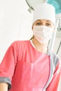 Close-up portrait of young female surgeon doctor in a pink medical gown with a face mask standing in operation theater Royalty Free Stock Photo