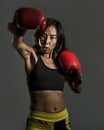 Close up portrait of young fit Asian Chinese woman in fitness top and boxing gloves throwing punch in bad girl attitude angry and Royalty Free Stock Photo