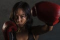 Close up portrait of young fit Asian Chinese woman in fitness top and boxing gloves throwing punch in bad girl attitude angry and Royalty Free Stock Photo