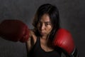 Close up portrait of young fit Asian Chinese woman in fitness top and boxing gloves throwing punch in bad girl attitude angry and Royalty Free Stock Photo