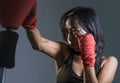 close up portrait of young fit Asian Chinese woman in fitness top and boxing gloves throwing punch in bad girl attitude angry