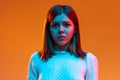 Close-up portrait of young girl standing with sad facial expression against orange studio background in neon light Royalty Free Stock Photo