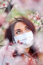 Close up portrait of young girl under a blossoming apricot tree with a mask from the coronavirus
