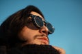 Close-up portrait of young guy with long hair wearing hipster round sunglasses and scarf. Blue sky on background. Down view. Royalty Free Stock Photo