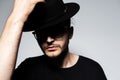 Close-up portrait of young handsome man wearing black hat and glasses on grey. Royalty Free Stock Photo