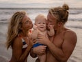 Close up portrait of young happy family spending time on the beach. Father and mother holding infant baby boy. Dad kissing their Royalty Free Stock Photo