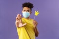 Close-up portrait of young hipster guy in medical mask stretch hand forward stop gesture, holding small paper crown