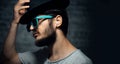 Close-up portrait of young hipster man, listen the music with wireless earphones, wearing cyan sunglasses and black hat. Royalty Free Stock Photo