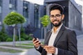 Close-up portrait of a young Indian businessman man sitting in a suit outside on a bench, holding a credit card and a Royalty Free Stock Photo