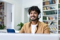 Close-up portrait of a young Indian male student in headphones studying in the library using a laptop Royalty Free Stock Photo