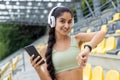 Close-up portrait of a young Indian woman in headphones doing sports, standing in a stadium, holding a phone in her hand Royalty Free Stock Photo