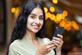 Close-up portrait of a young Indian woman standing on a city street in the evening, holding a phone and smiling at the Royalty Free Stock Photo