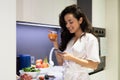 Close up portrait of young joyful Caucasian woman in white robe smiling and looking at gadget screen standing in kitchen Royalty Free Stock Photo