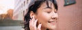 Close up portrait of young korean woman touches earphone, listens music in headphones with pleased smiling face, walks Royalty Free Stock Photo