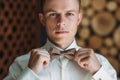 Close-up portrait of young male businessman is getting dressed for work. A blond guy in a white shirt is trying on a bow